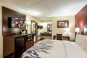 Een hotelkamer met een bed, een bureau, een televisie, een spiegel en een badkamer.
