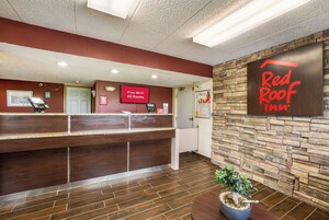 Un área de recepción con el letrero de Red Roof Inn, una pantalla digital que indica Wi-Fi gratuito y un mostrador de recepción con una computadora y un teléfono.
