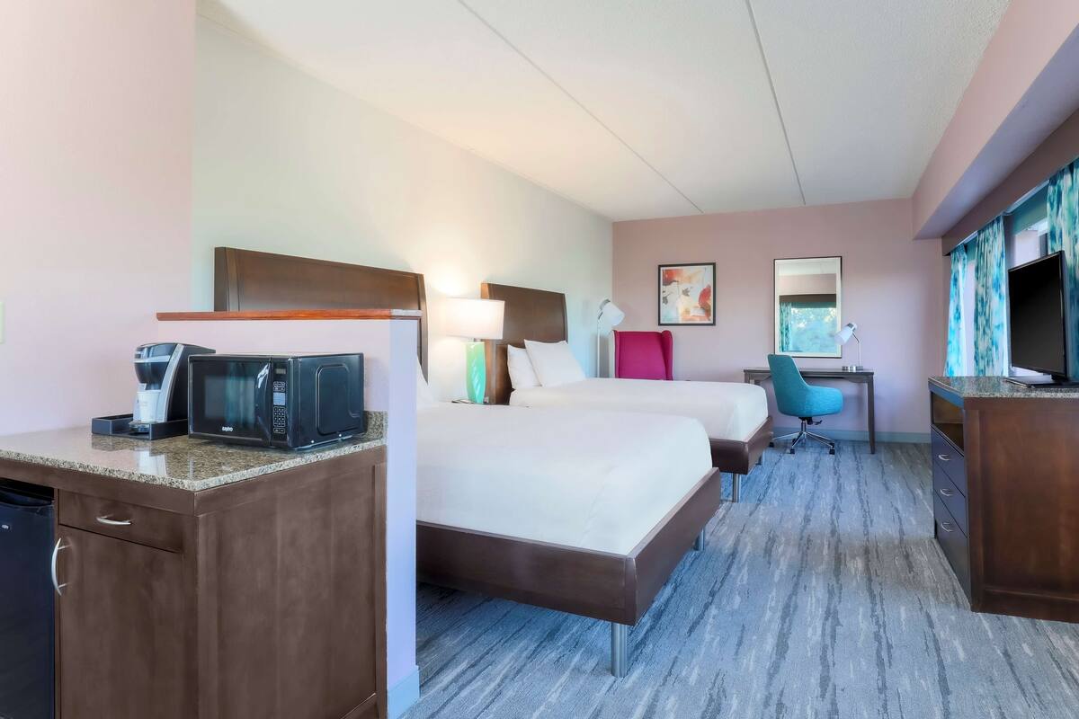 A hotel room with a bed, a desk, a chair, a microwave, and a TV.
