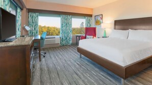 A hotel room with a bed, desk, chair, and a view of trees through the window. - Hilton Garden Inn Raleigh-Durham/Research Triangle Park (Durham)