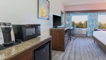 Una habitación de hotel con kitchenette, televisión, escritorio y cama.