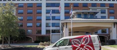 A Hilton Garden Inn with a modern building facade, a parking area, and a service van.