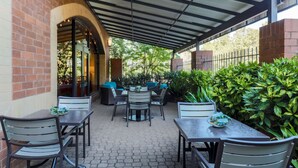 An outdoor patio with hexagonal tile flooring, covered by a metal roof, and furnished with tables and chairs. - Hilton Garden Inn Raleigh-Durham/Research Triangle Park (Durham)
