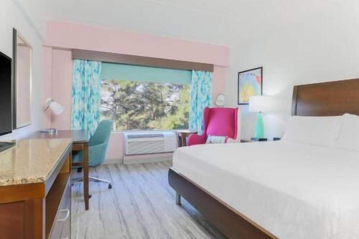 A hotel room with a bed, desk, chair, and a window with curtains.