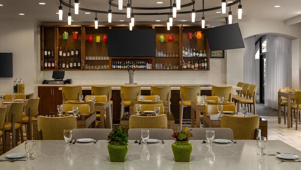 A restaurant with a bar area, yellow chairs, and tables set for dining. - Hilton Garden Inn Raleigh-Durham/Research Triangle Park (Durham)