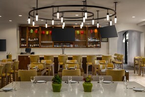 A restaurant with a bar area, yellow chairs, and tables set for dining. - Hilton Garden Inn Raleigh-Durham/Research Triangle Park (Durham)