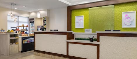 A hotel reception area with a counter, a refrigerator, and a display of snacks.