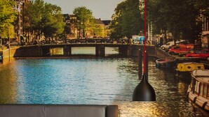 A hotel room with a bed, a nightstand, and a view of a canal with boats and a bridge. - Swissôtel Amsterdam (Amsterdam)
