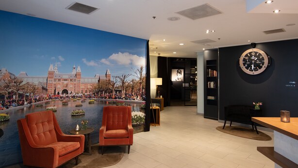 A lobby with a large mural of a historic building, two armchairs, a round table, and a wall clock. - Swissôtel Amsterdam (Amsterdam)