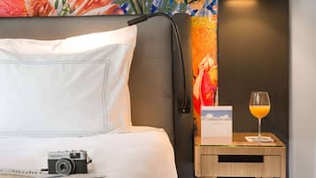 A hotel room with a bed, a nightstand with a lamp, a camera, a glass of orange juice, and a menu.