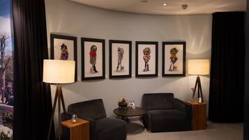 A modern hotel room with a curved ceiling, a large window with a view of a cityscape, a seating area with two armchairs and a small round table, and a wall decorated with framed artwork.