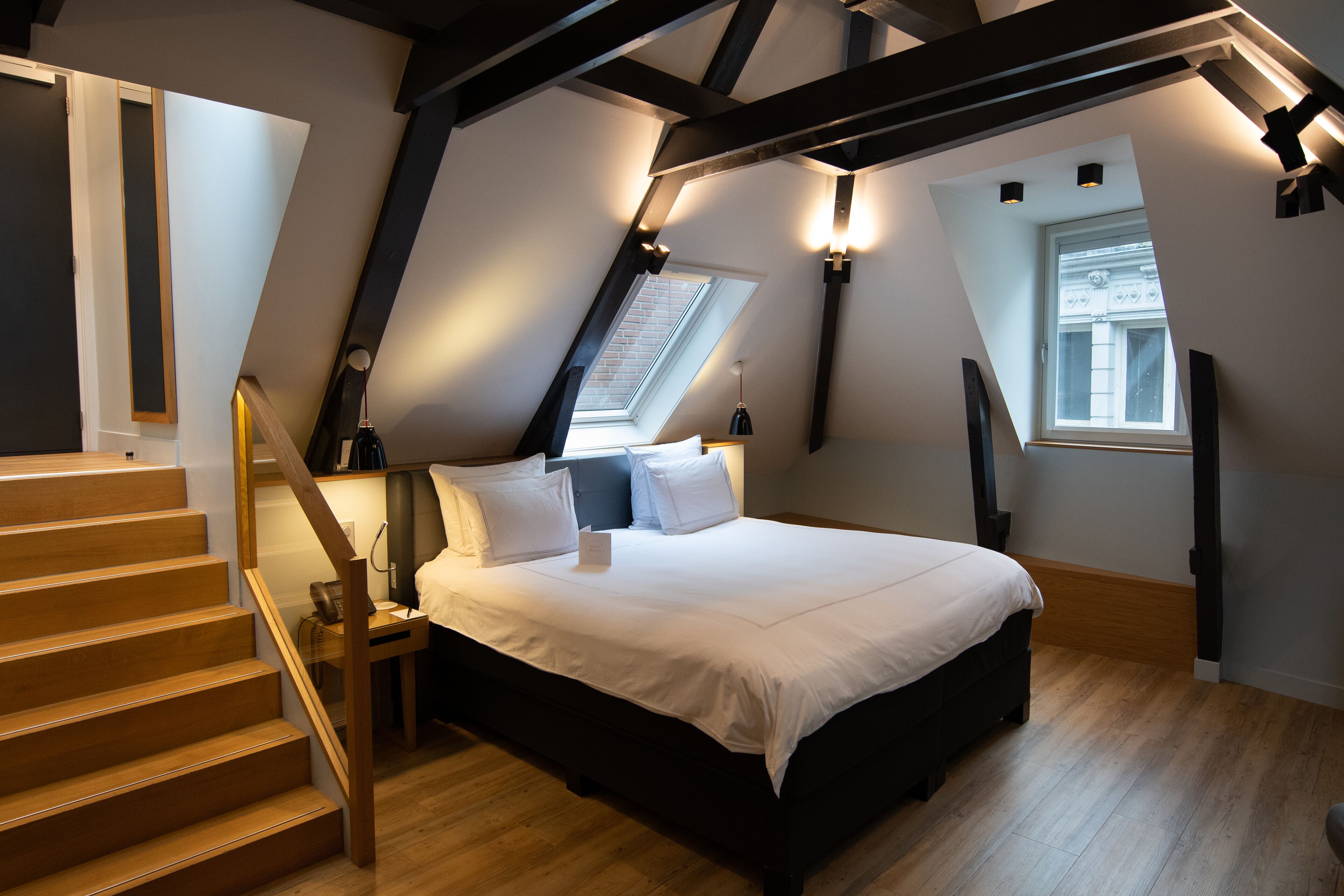 A bedroom with a bed, a wooden staircase, and a skylight.