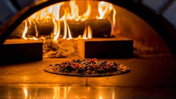 A pizza oven with a fire burning inside, and a pizza on the counter in front of it.