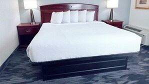 Habitación de hotel con una cama grande, dos mesitas de noche con lámparas, aire acondicionado de pared y un cuadro enmarcado.