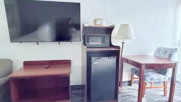 Habitación compacta con televisión de pantalla plana, microondas, refrigerador, una mesita y un sofá.