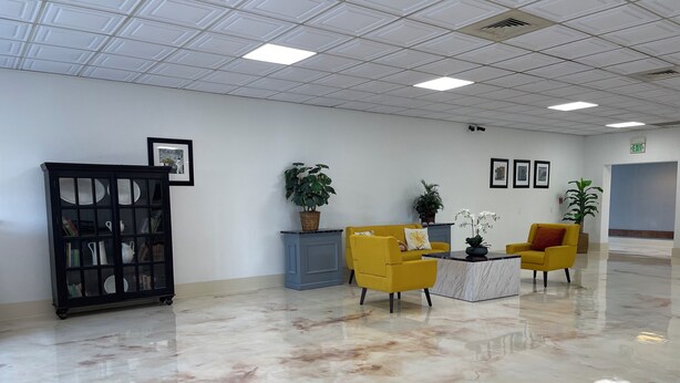 Un vestíbulo amplio con piso de mármol, un gabinete negro con puertas de vidrio, sillones amarillos y una consola azul.