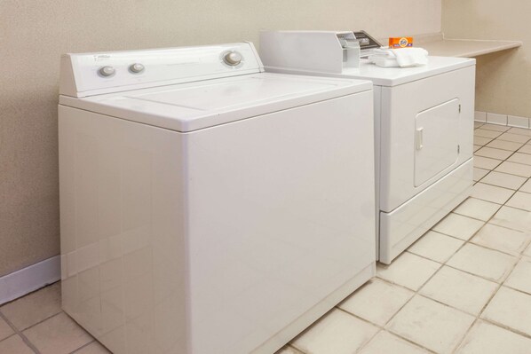 A laundry area with a front-loading washer and dryer, a shelf with laundry supplies, and a tiled floor.