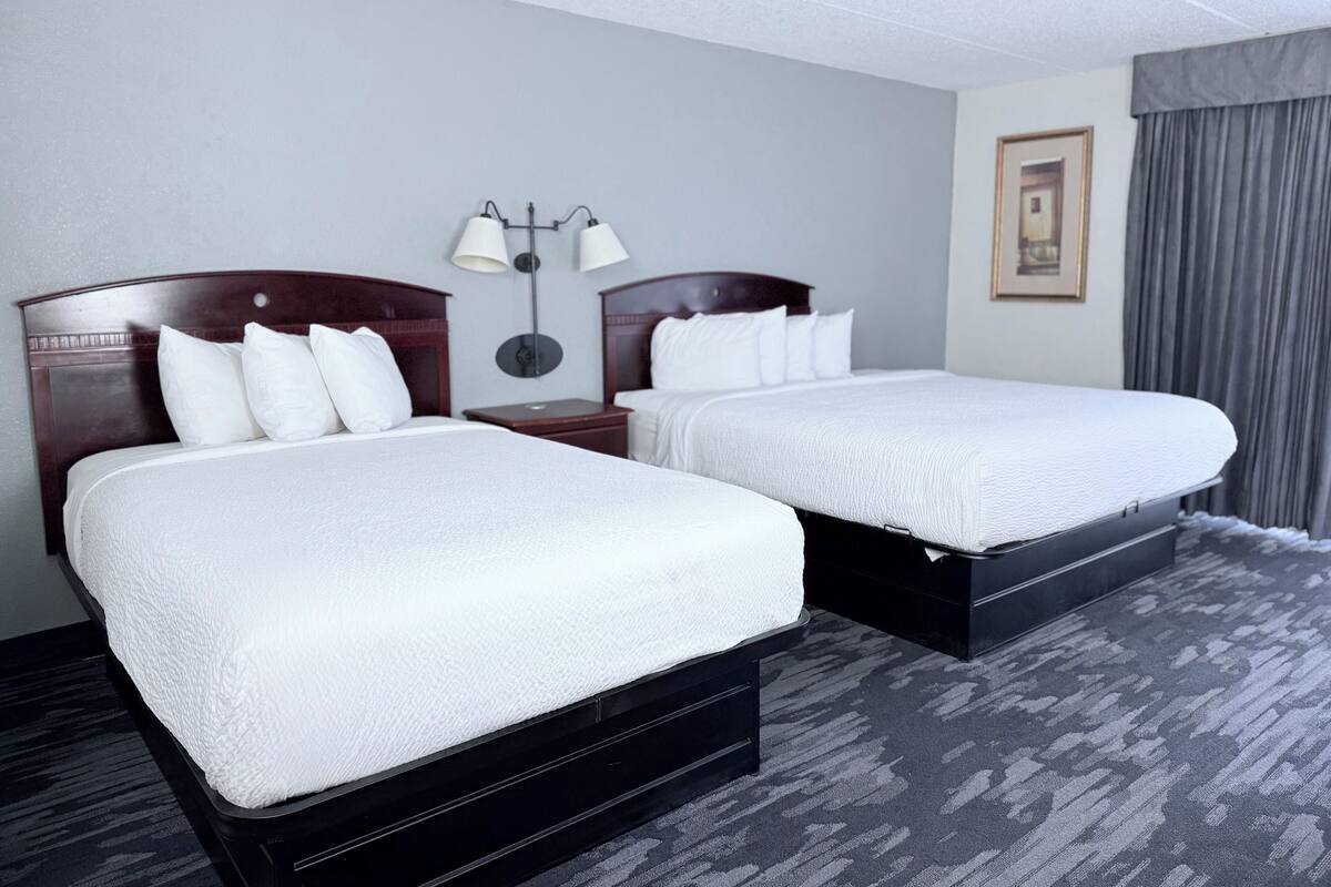 A hotel room with two beds, a nightstand, a lamp, and a framed picture on the wall.