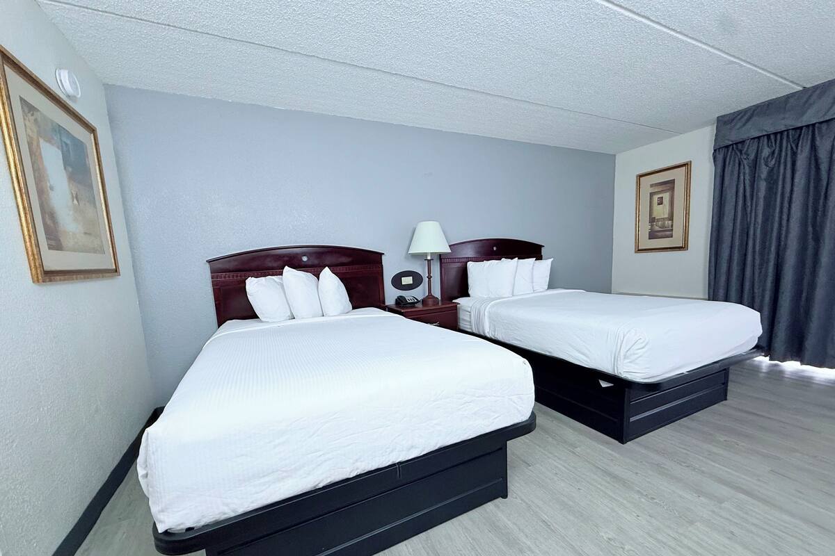 A hotel room with two beds, a nightstand with a lamp, and a framed picture on the wall.