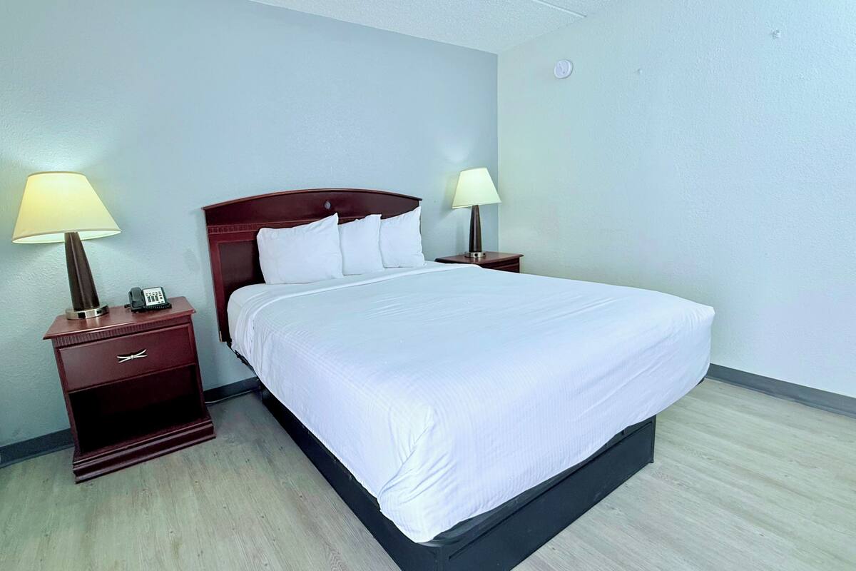 A neatly made bed in a hotel room with a wooden headboard, two bedside tables with lamps, and a plain wall.