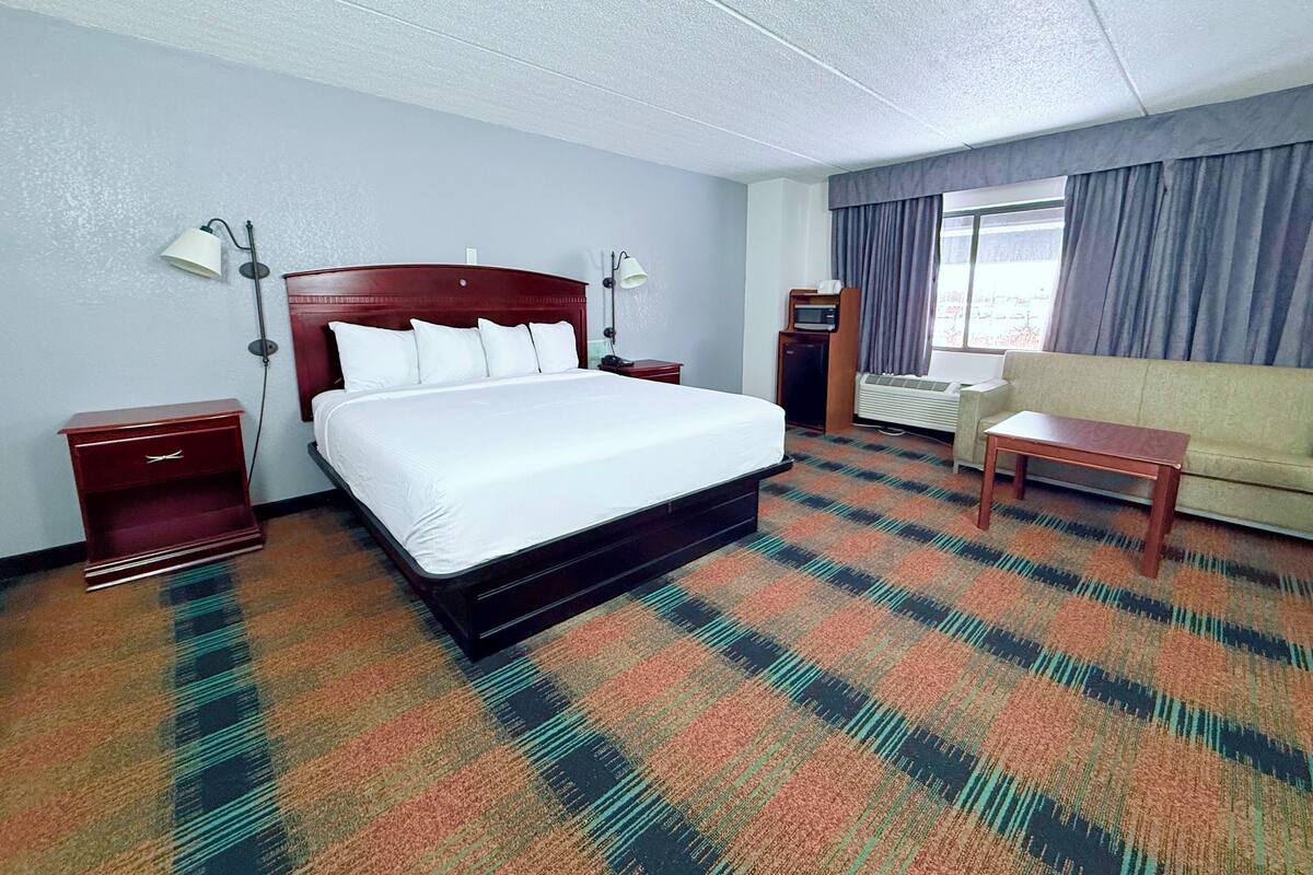 A hotel room with a large bed, a sofa, a desk, and a window with curtains.