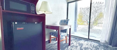 Habitación de hotel con refrigerador, lámpara, mesa y vistas al exterior.