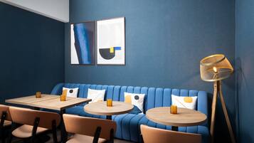 A modern restaurant interior with blue walls, a blue sofa, wooden tables, and orange chairs.