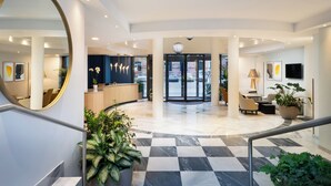 A modern hotel lobby with a checkered floor, a reception desk, seating area, and a large mirror. - voco Vienna Prater by IHG (Vienna)