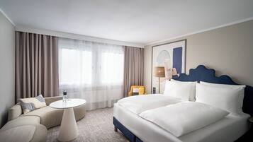 A hotel room with a bed, a sofa, a small round table, and a lamp.