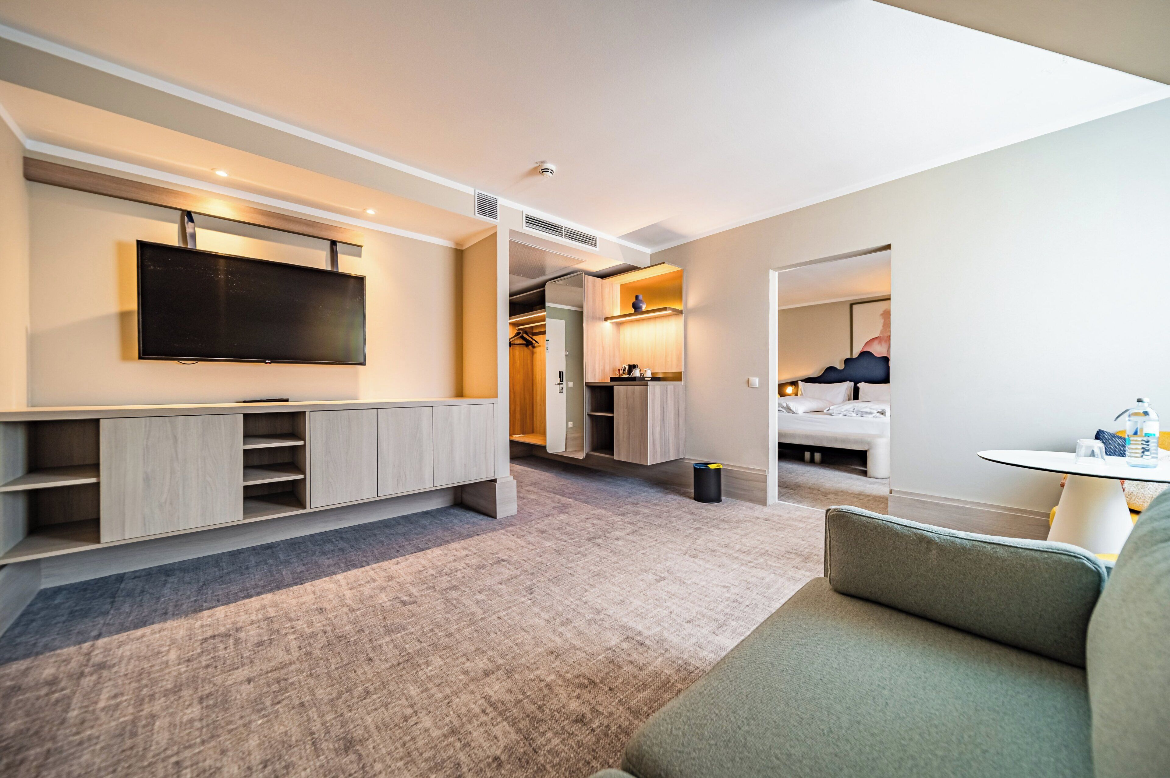 Une chambre d’hôtel moderne équipée d’une télévision à écran plat, d’un coin salon, d’une kitchenette et d’une salle de bain.