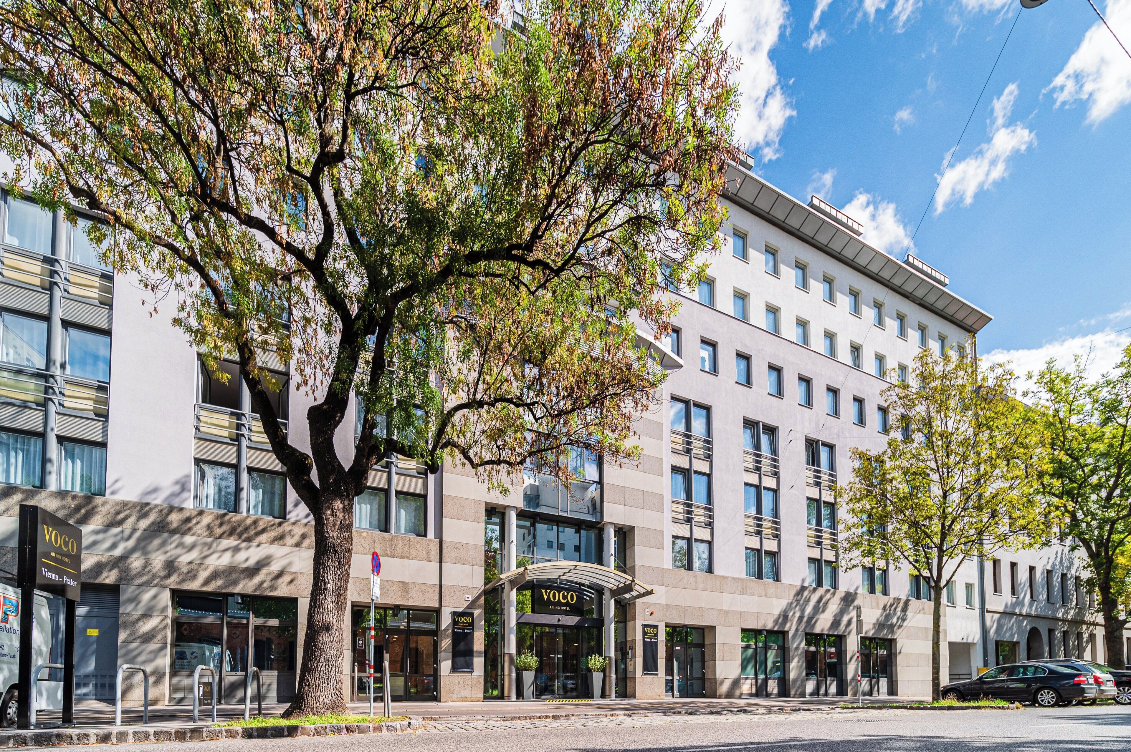 Ein modernes Hotelgebäude mit markanter Fassade, großen Fenstern und einem Baum davor.