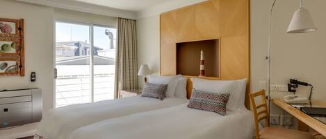 A hotel room with two beds, a desk, a chair, a lamp, and a view of the outside.