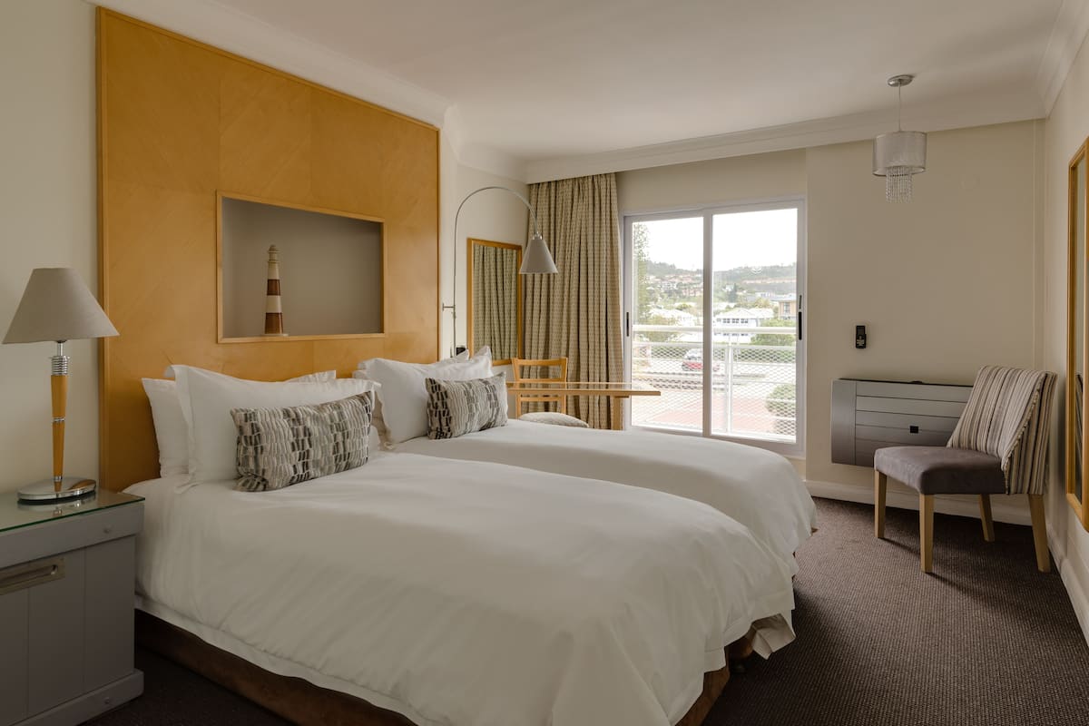 Habitación de hotel con dos camas, un escritorio, una silla, una lámpara, un ventanal y vistas al exterior.