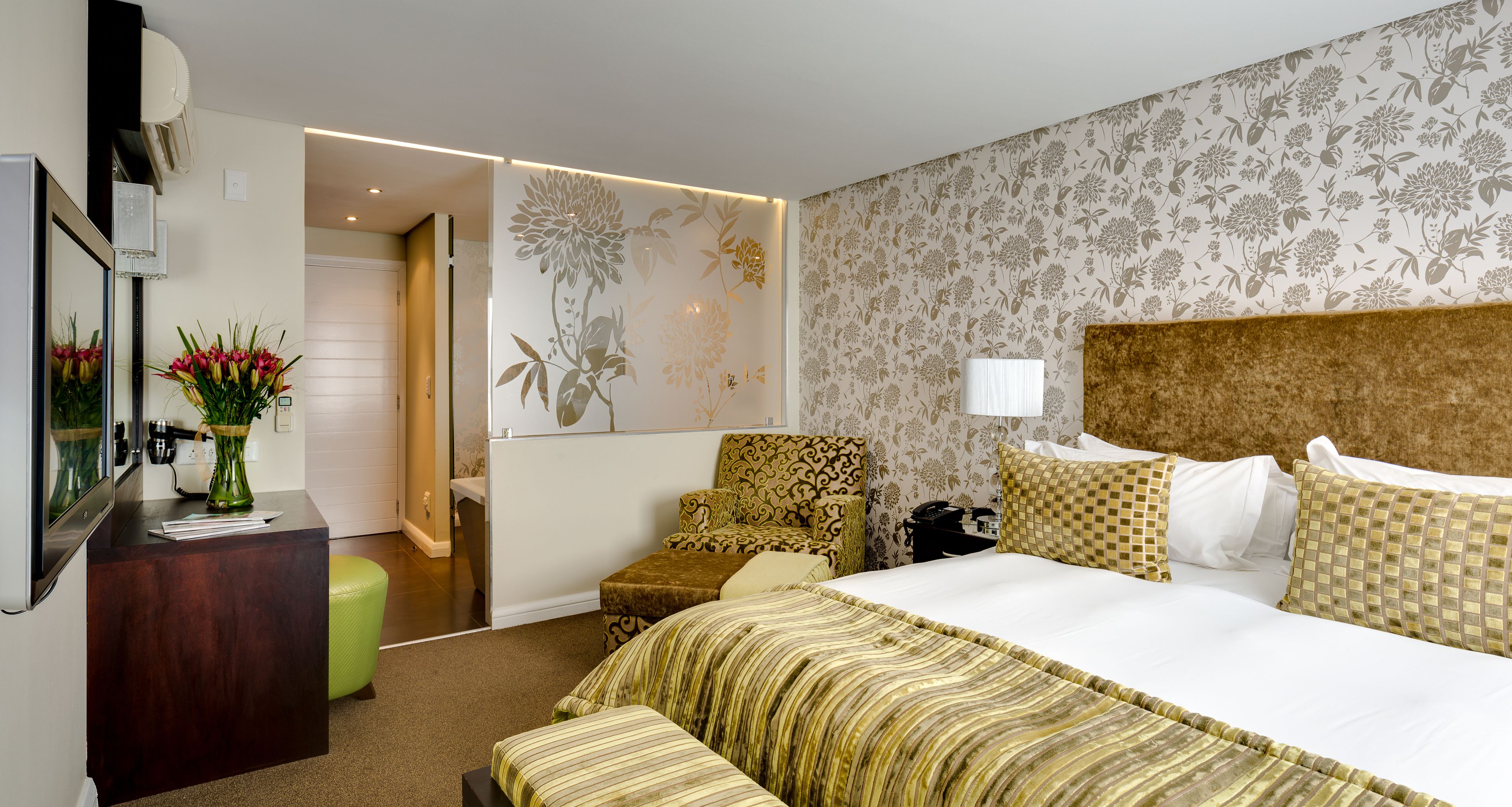 A hotel room with a large bed, a desk with a vase of flowers, a chair, and a mirror.