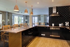 Een moderne keuken met een zwarte achterwand, roestvrijstalen apparatuur en houten stoelen.