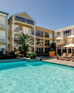 Een hotel met een zwembad, terras en een bordje met de tekst 'Protea Hotel Knysna Quays'.