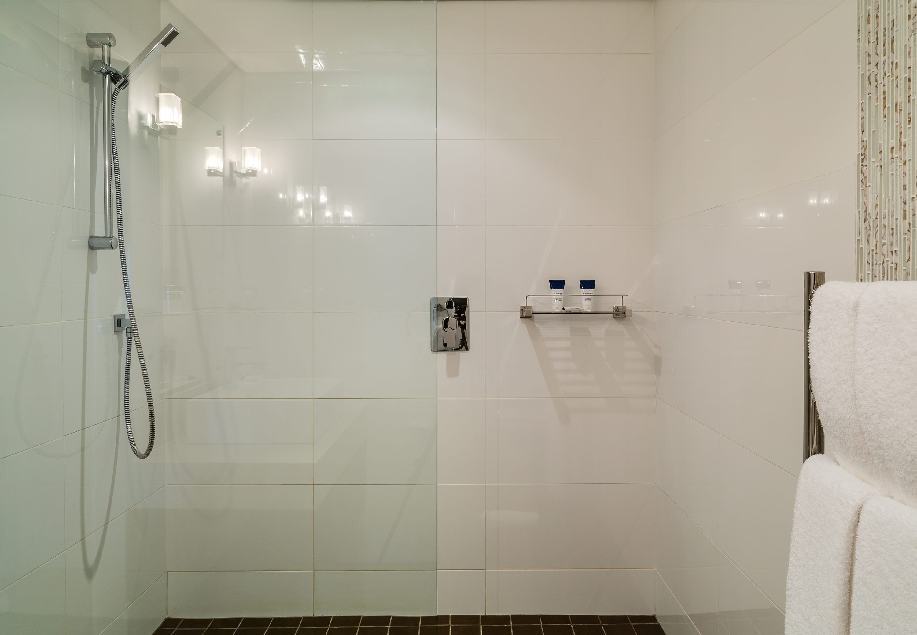 Un baño moderno con cabina de ducha de vidrio, un perchero y un estante pequeño con artículos de aseo.