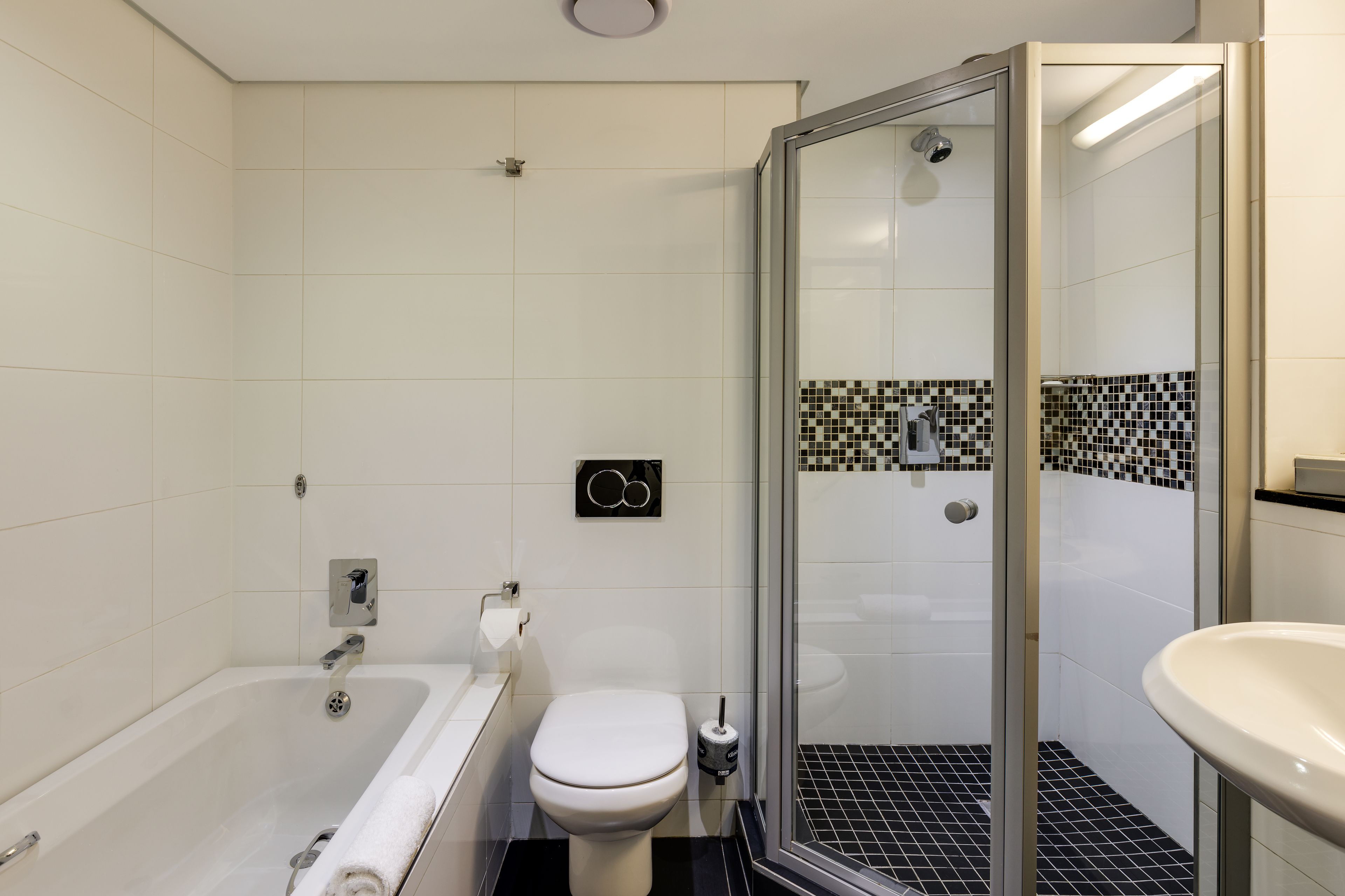 A modern bathroom with a bathtub, toilet, and glass-enclosed shower.