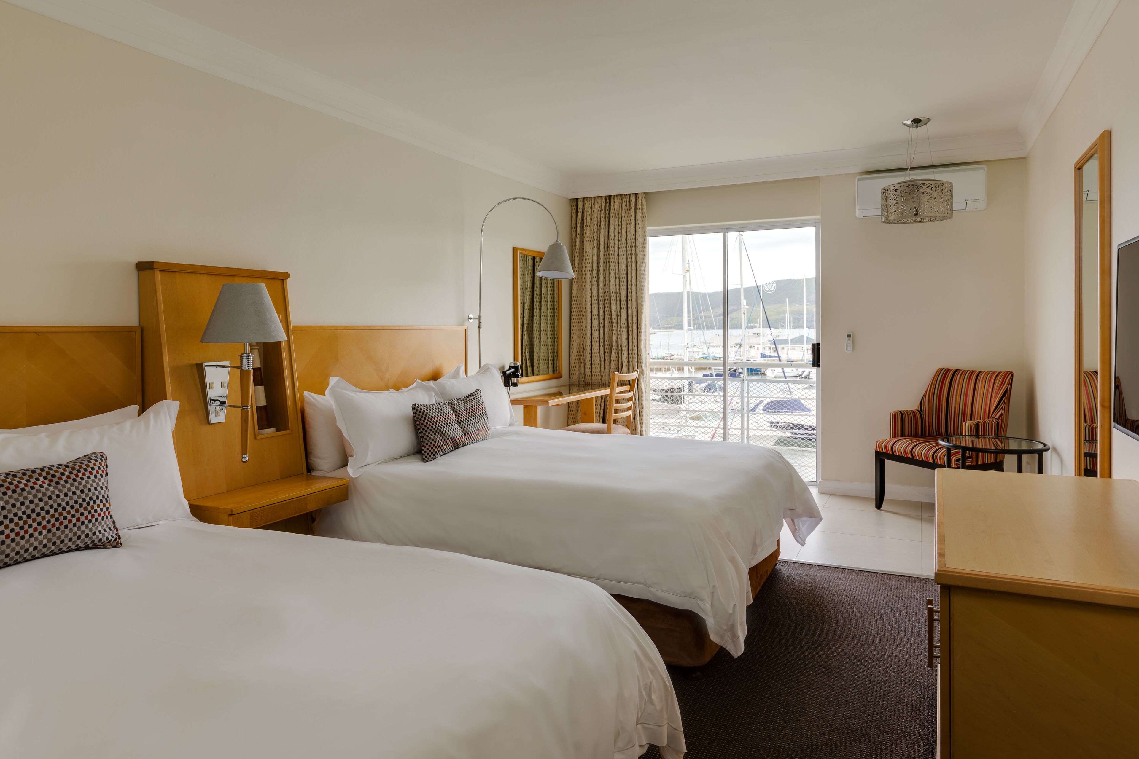 Une chambre d’hôtel avec deux lits, un bureau, une chaise et une vue sur le port de plaisance.