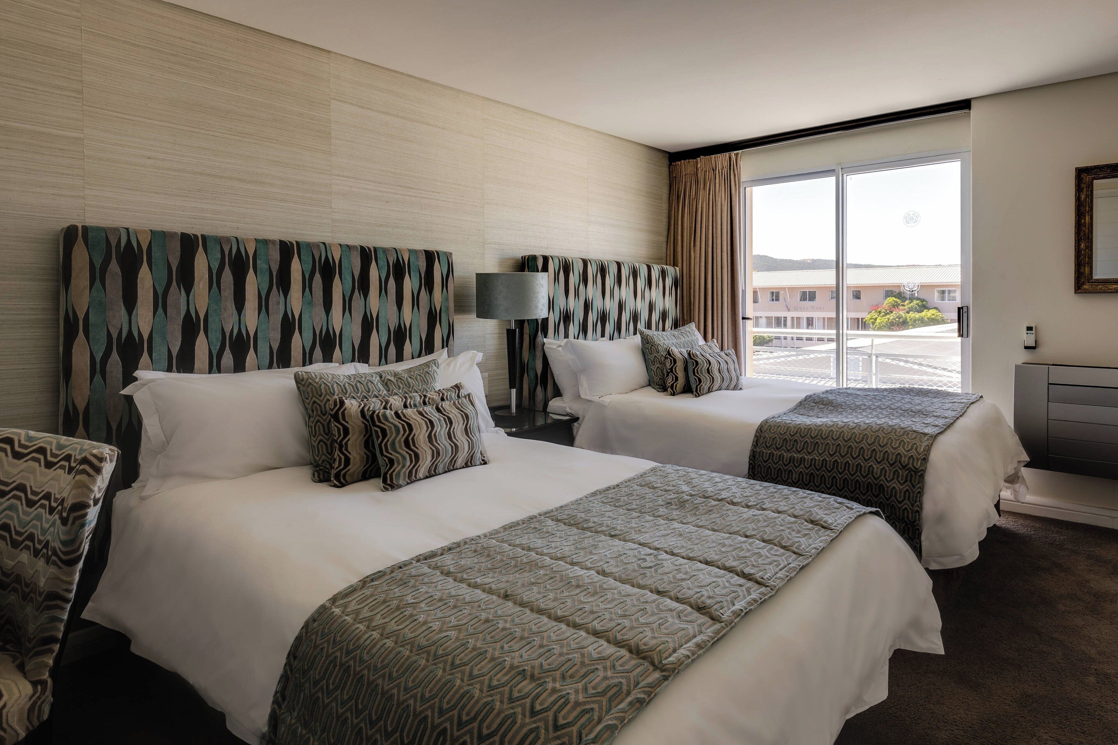 A hotel room with two beds, a large window, and a view of the outside.
