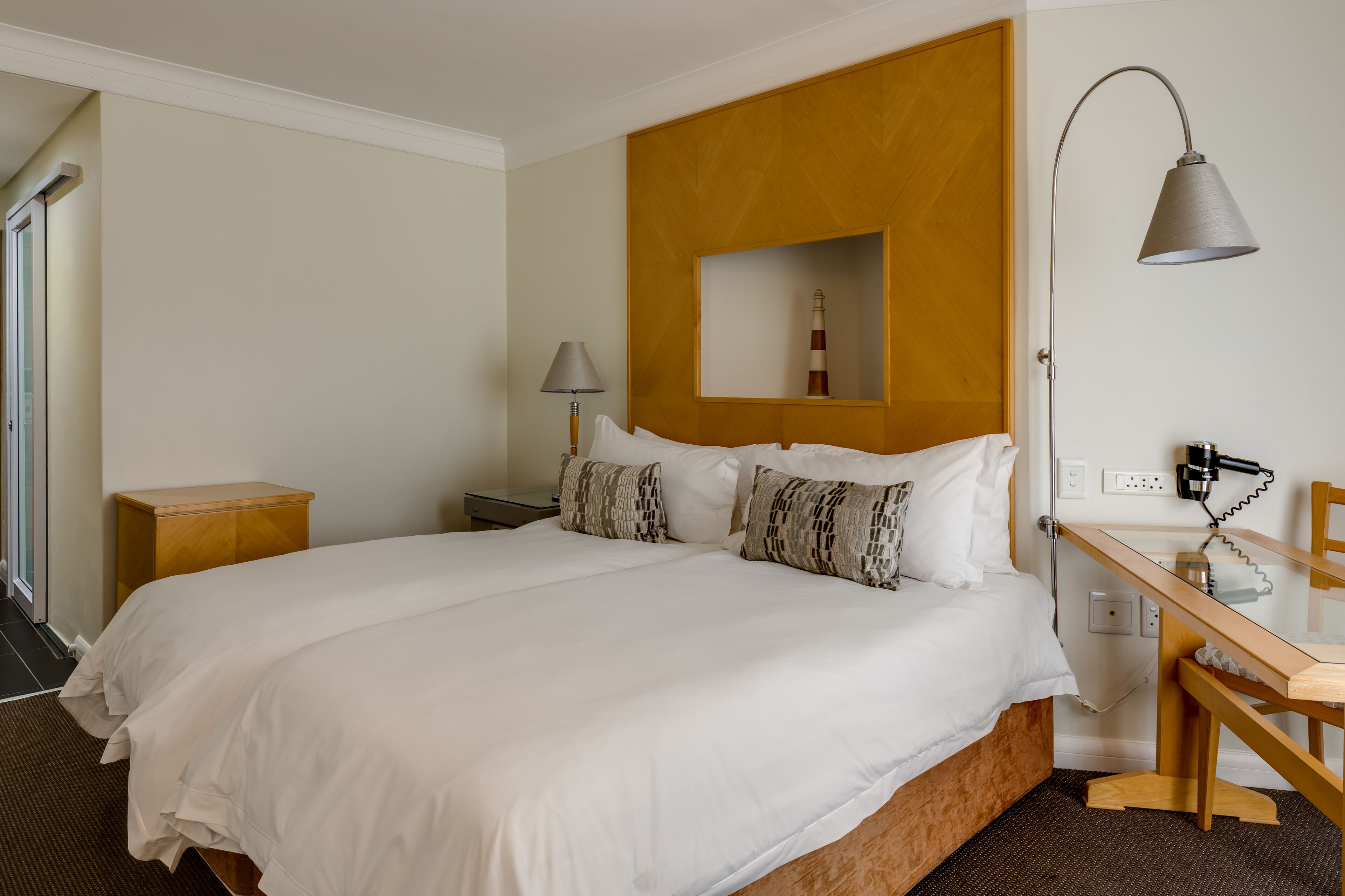 A hotel room with a large bed, a wooden desk, a lamp, and a mirror.