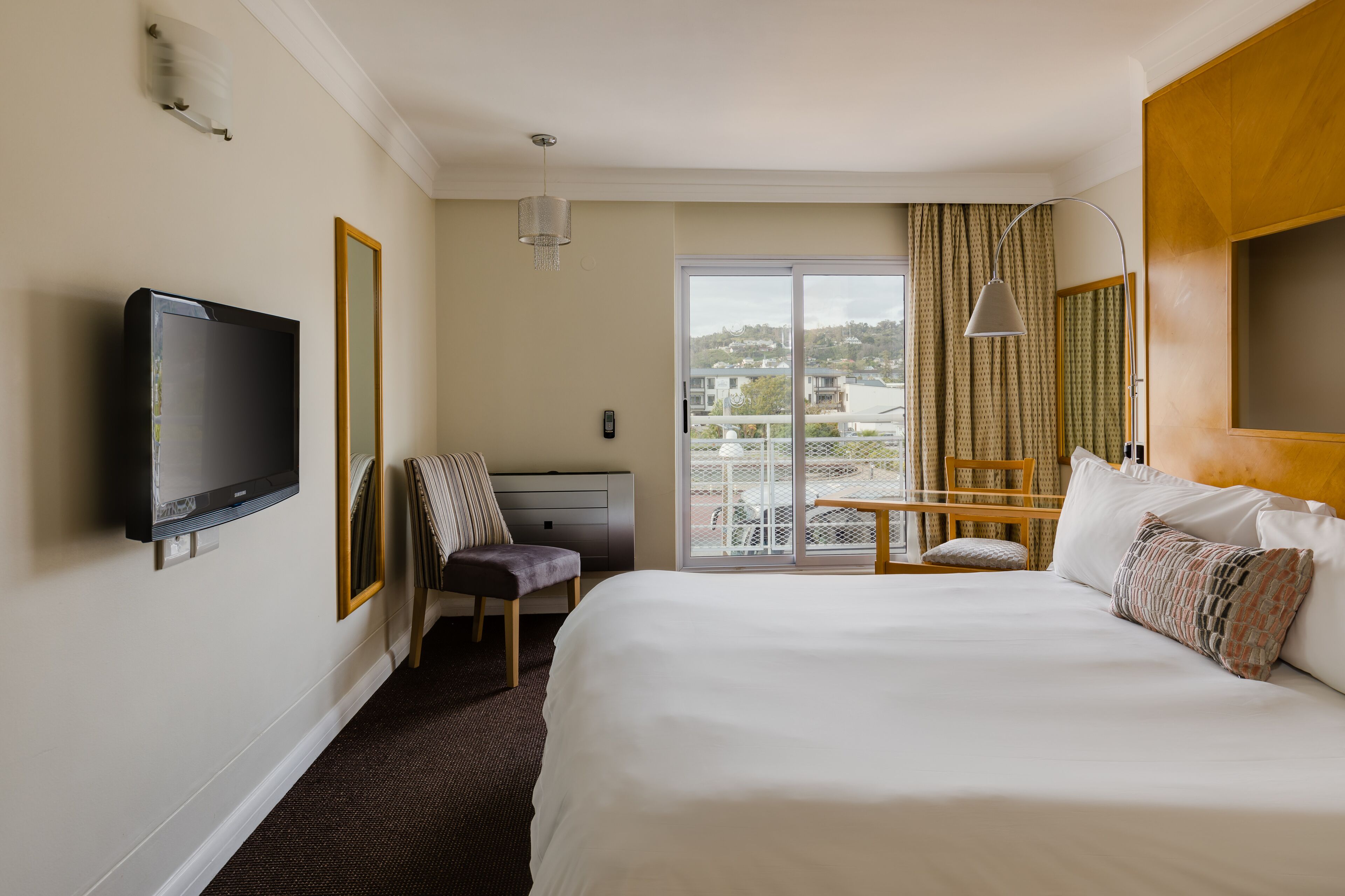Hotelkamer met een groot bed, een aan de muur bevestigde televisie, een bureau met stoel, en uitzicht door een schuifdeur.