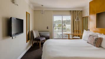 A hotel room with a large bed, a television mounted on the wall, a desk with a chair, and a view through a sliding glass door.