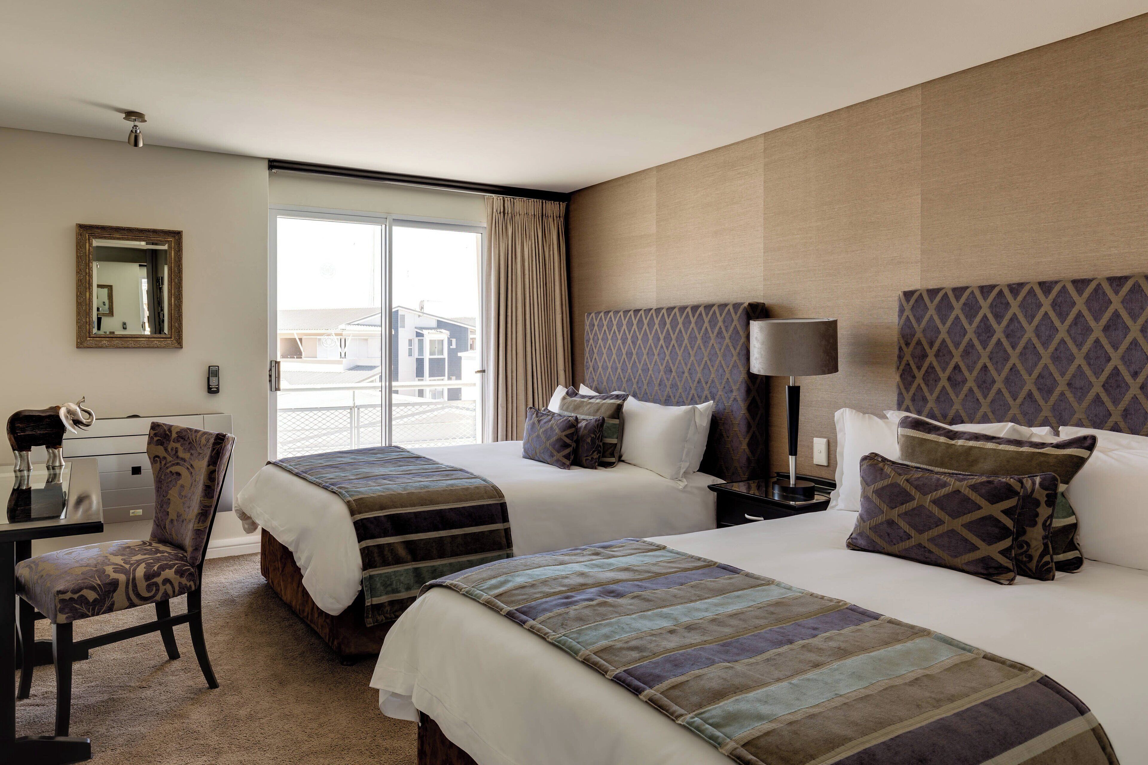 A hotel room with two beds, a desk, a chair, and a large window.