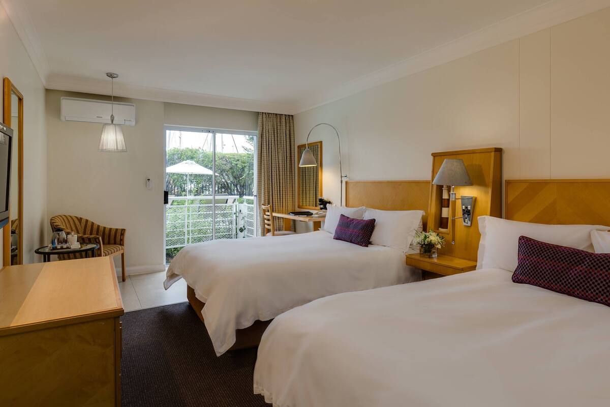 Habitación de hotel con dos camas, un escritorio, una silla y un balcón con vistas.