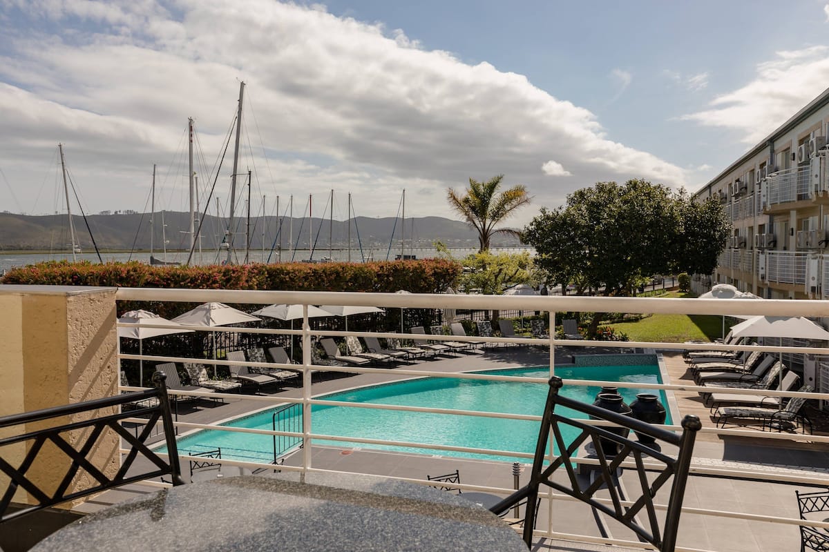 Zona de piscina en la azotea con sillones de descanso y sombrillas, con vistas a una masa de agua con veleros.