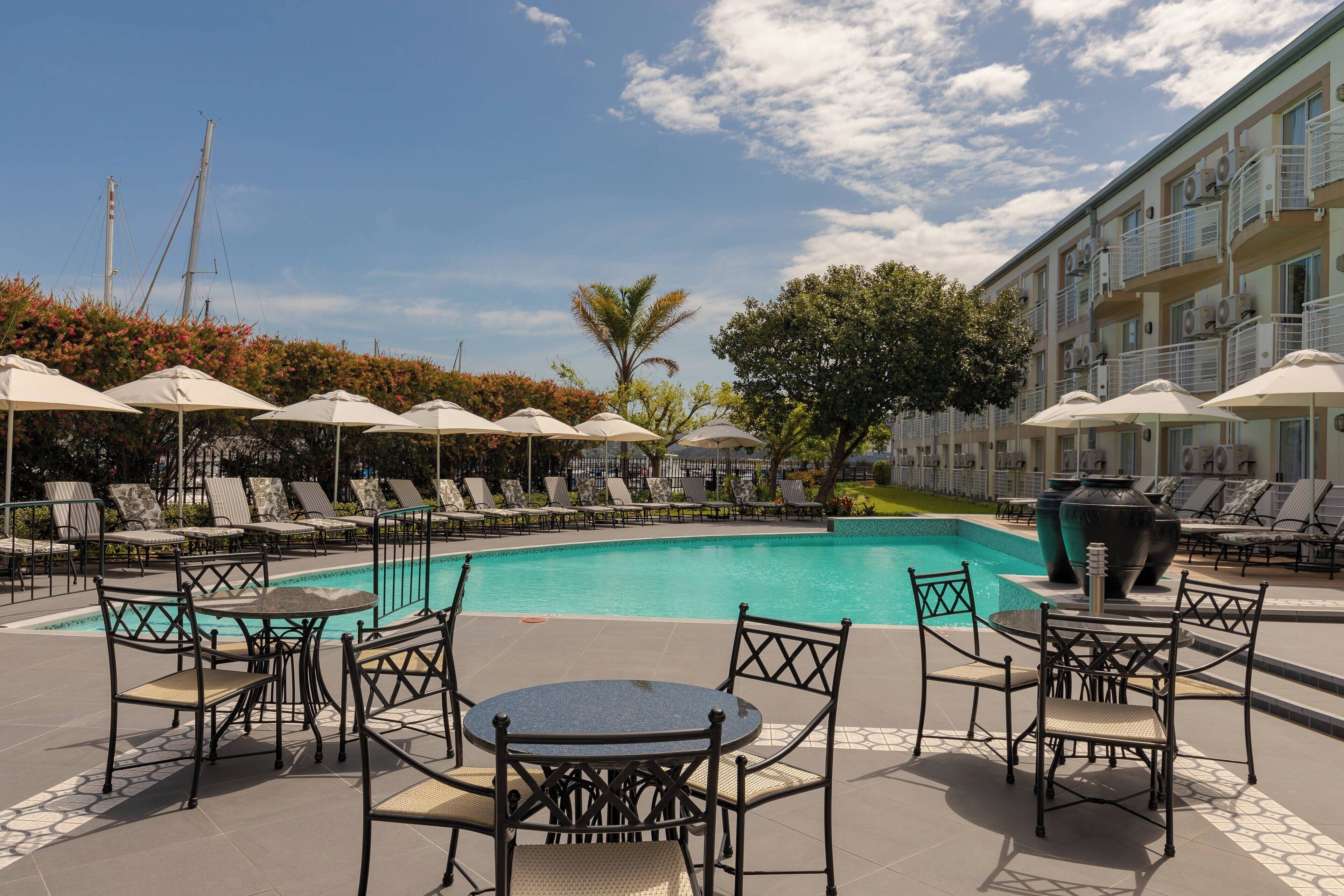 Zona de piscina con sillones de descanso y sombrillas, una piscina y un edificio con balcones.