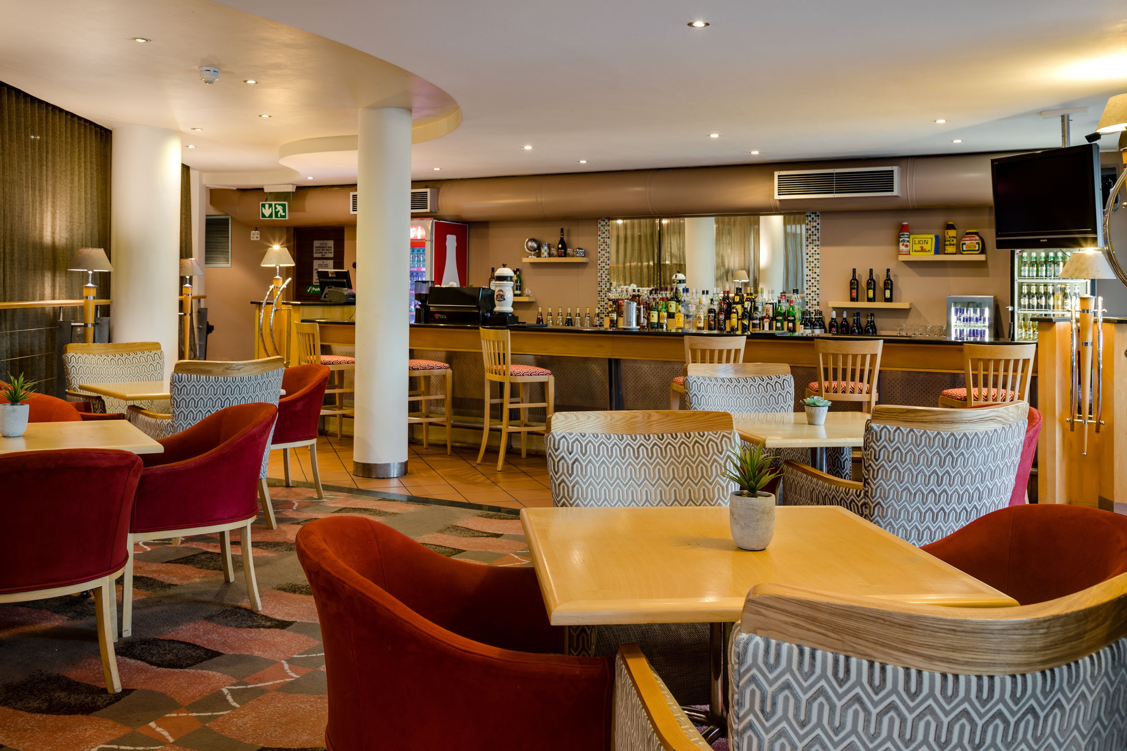 Een hotel lobby met een bar, zitgedeelte en een televisiescherm.