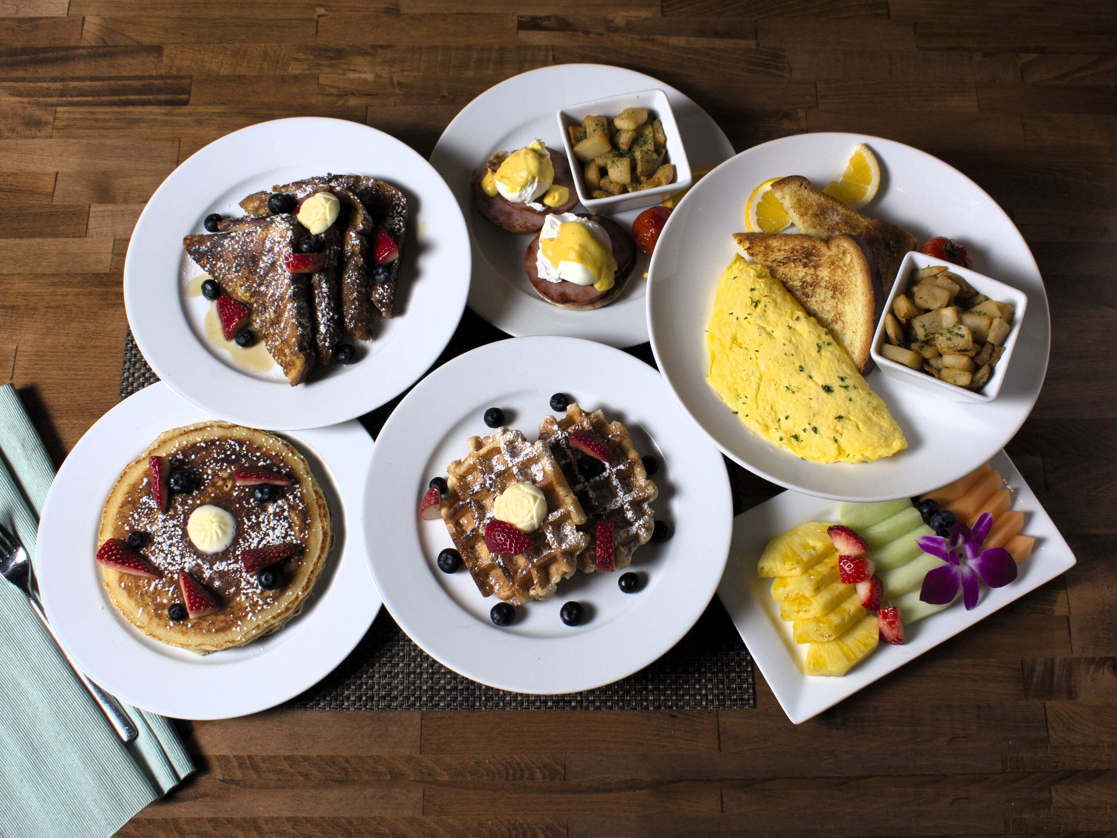 Ein reichhaltiges Frühstücksbuffet mit Pfannkuchen, Waffeln, Eiern und Obst auf weißen Tellern.