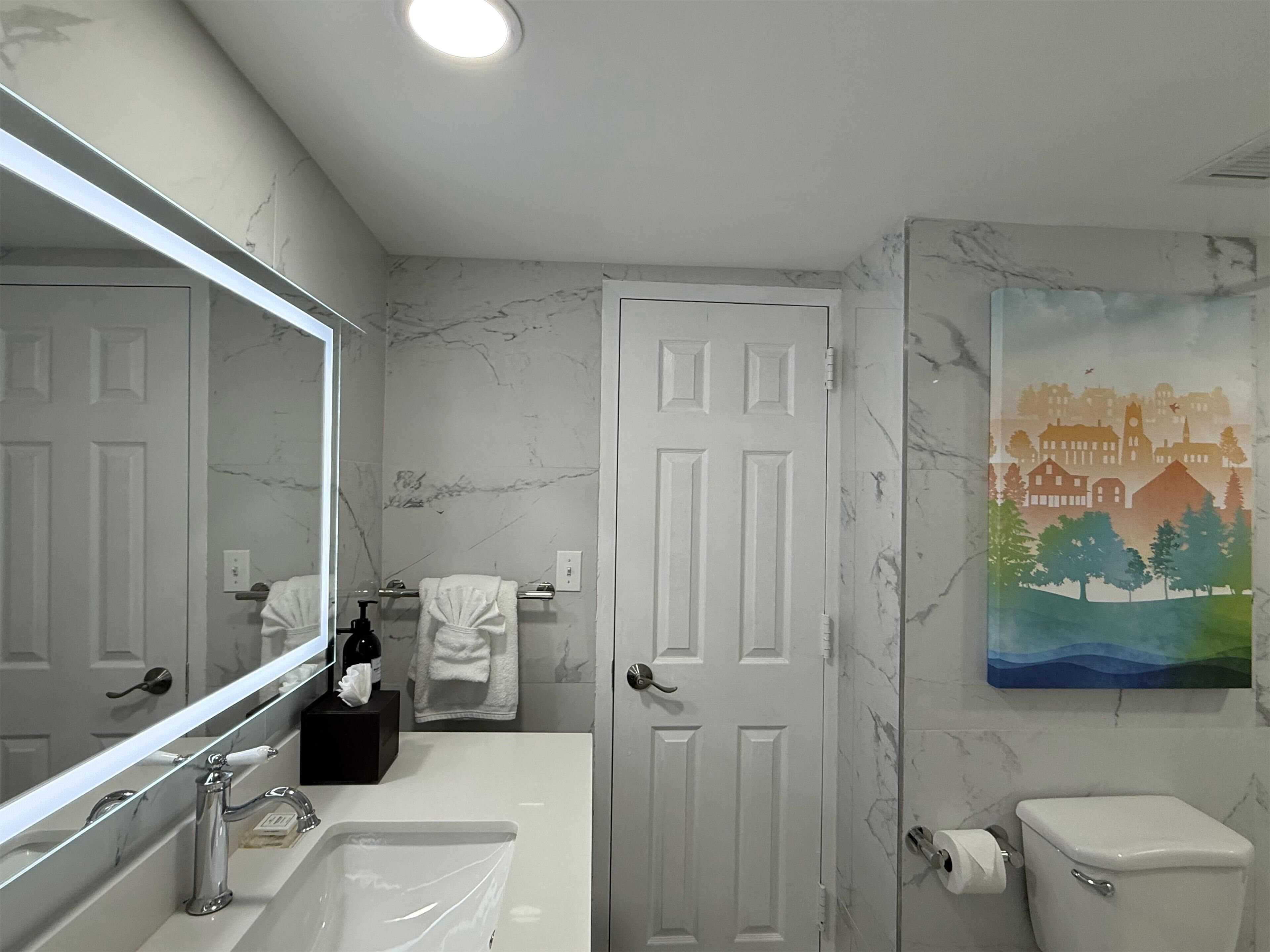 A bathroom with a white door, a sink, a toilet, and a mirror.